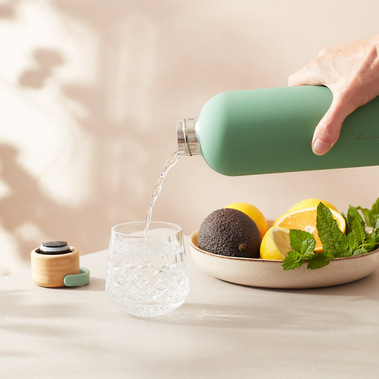 Food photography, water being poured from a bottle into a glass on a light beige background