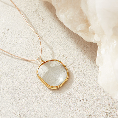 Jewellery photography of a gemstone pendant on a textured background with a piece of natural crystal