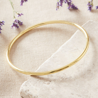 A gold bangle photographed on a textured linen background with dried flowers 