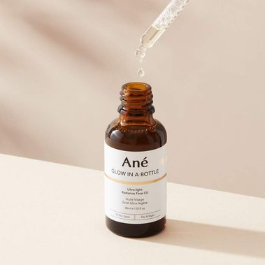 A glass dripper containing a facial serum on a neutral background