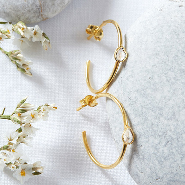 Boho jewellery photography of gold and diamond earrings on a white linen and stone background