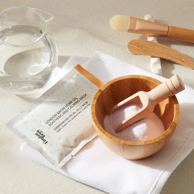 Skincare product photography.  A powder hemp oil face mask being prepared in a bowl, with applicators and water jug