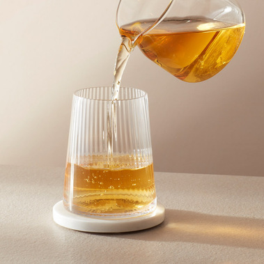 Tea product photography.  A cold brew tea being poured into a glass from a glass teapot, minimal props and a neutral background