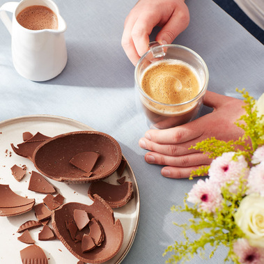 Hot chocolate being held in a mug with Easter egg chocolate on a plate