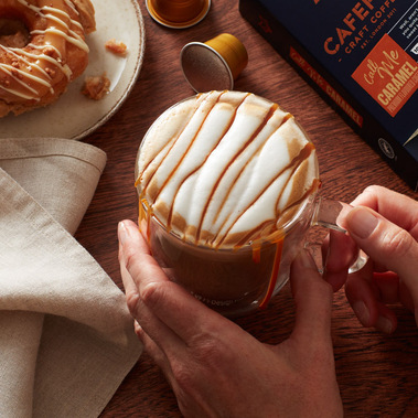 A glass mug of caramel coffee being hand held