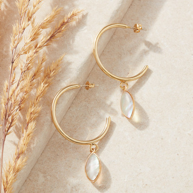 Jewellery photography of a pair of gold hoop earrings on a beige stone background