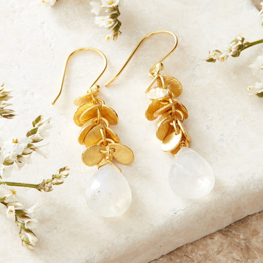 Lifestyle jewellery photography of gemstone gold earrings on a white textured stone surface with fresh flowers