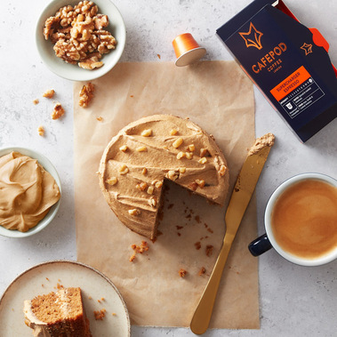 Flat lay of a coffee cake surrounded by ingredients and a fresh coffee on a neutral background