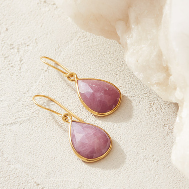 Jewellery photography of gold ruby earrings on a rough textured beige background