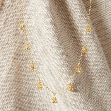 Boho gold necklace hung over natural coloured linen fabric 