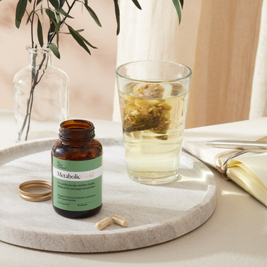 Supplement capsules with the bottle besides a glass herbal tea cup