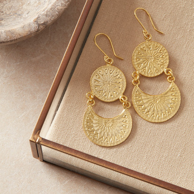 Gold boho earrings in a glass jewellery box on a linen background