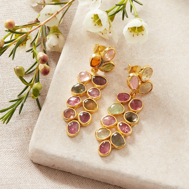 Boho jewellery photography of tourmaline gold earrings on a beige stone surface with fresh flowers