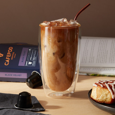 Iced coffee in a glass with a straw next to a cinnamon bun 
