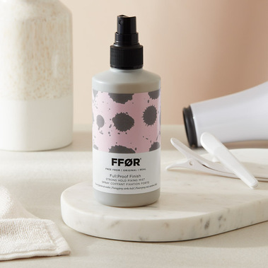Haircare product photography, spray bottle on a marble tray with a hairdryer in the background.