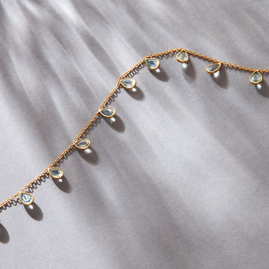 Jewellery photography, a gold gemtsone necklace on a grey background with daylight shadows