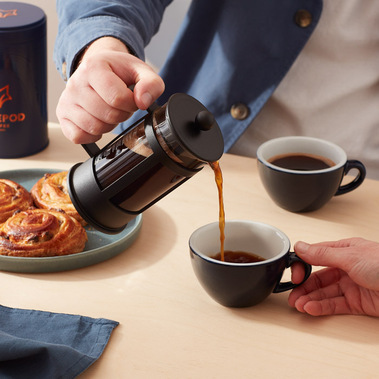 Coffee product photography.  Coffee being poured from a cafetière into a cup on a neutral tabletop