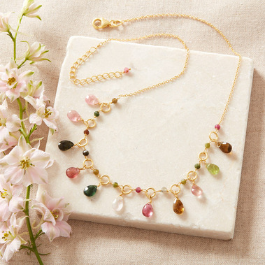 Jewellery photography, gold gemstone necklace on a neutral stone background with fresh flowers.