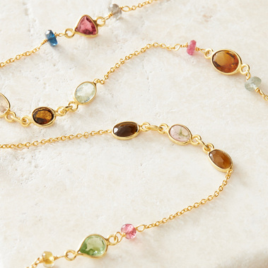 Jewellery photography, gold gemstone necklace on a neutral stone background.