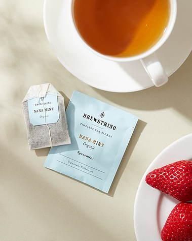 A cup of tea with a plate of strawberries on a neutral background with daylight shadows
