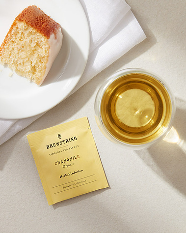 A cup of tea with a slice of cake on a neutral background with daylight shadows