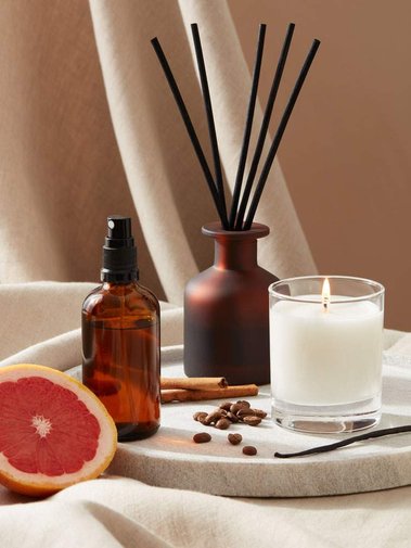 Product photography of a candle, diffuser and room spray with ingredients on a beige linen fabric background