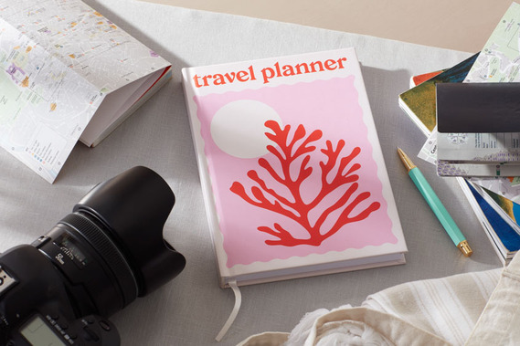 Stationery photography, a travel planner on a grey tabletop surrounded by guidebooks and a camera