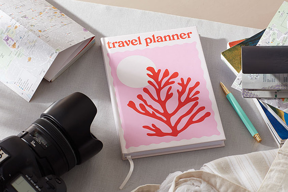 Stationery photography, a travel planner on a grey tabletop surrounded by guidebooks and a camera
