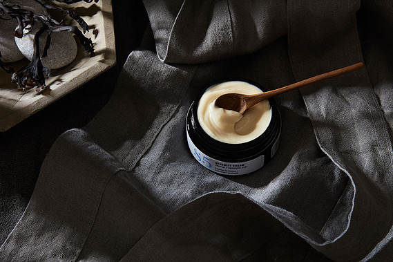 An open jar of skincare moisturiser on a dark moody grey background. Beauty product photography 