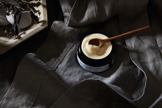 An open jar of skincare moisturiser on a dark moody grey background. Beauty product photography 