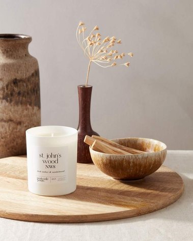 Product photography of a scented candle with ingredients of sandalwood on a wooden platter with dried flowers and vases