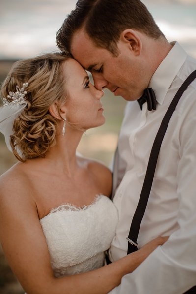 Braut und Bräutigam sind ganz dich mit Gesichter an einander, er trägt Hosenträger und Sie ein trägerlose Hochzeitskleid und Schleife in den Haaren