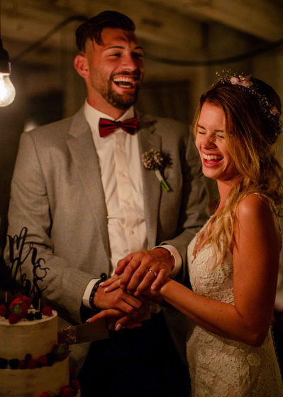 Das Brautpaar schneidet die Hochzeitstorte an  mit viel Freude und Lachen im natürlichen Kerzenlicht 