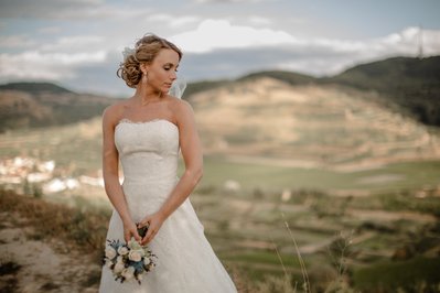 Braut im Hochzeitskleid in auf dem Berg in den Regen am Kaiserstuhl und hält einen Brautstrauß in beiden Händen aus hellen Blumen 