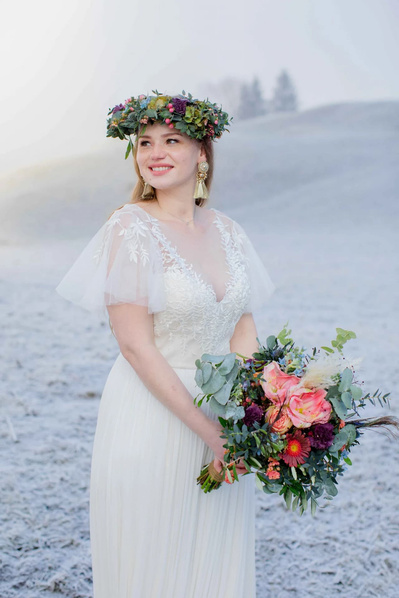 Braut im Winterlandschaft mit wunderschönen Blumenstrauß und Blumenkranz auf dem Kopf