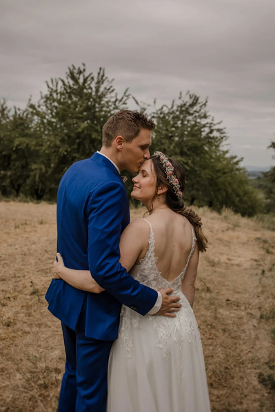 Bräutigam im blauen Anzug umarmt seine Braut in der Natur