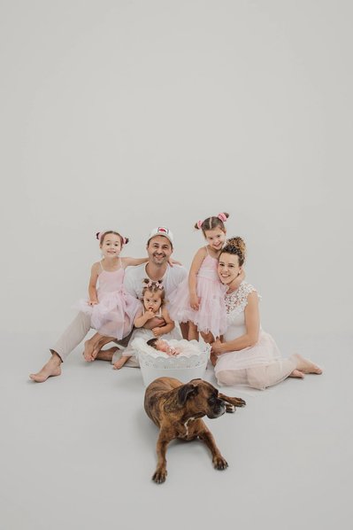 Familienfoto im Fotostudio auf dem Bett mit Geschwister in rosa Kleider  und mit einem Hund