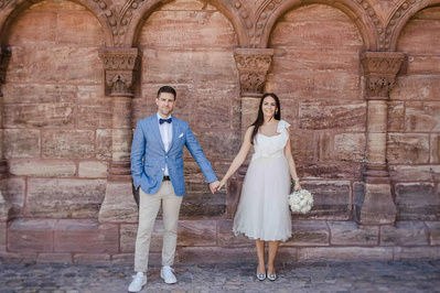 Bräutigam in blauen Sakko und beige Hose und Braut ein einem zartem Kleid und offene Haare  für Fotoshooting vor dem Münster in Basel