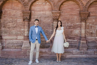 Bräutigam in blauen Sakko und beige Hose und Braut ein einem zartem Kleid und offene Haare  für Fotoshooting vor dem Münster in Basel