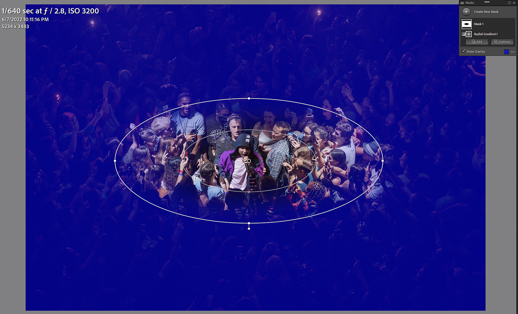 A screenshot of the Radial Gradient mask being applied to a concert photo in Adobe Lightroom. The overlay of what areas will be affected by the mask adjustments is shown in blue.
