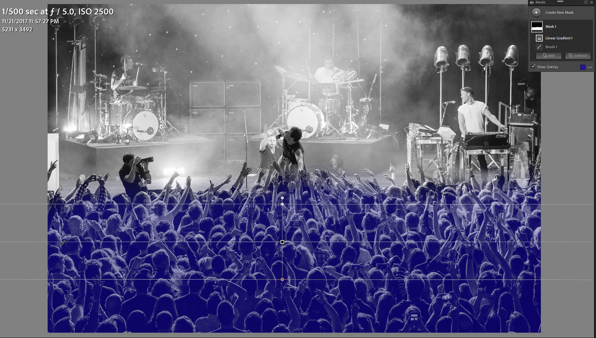 A screenshot of the Linear Gradient mask being applied to a concert photo in Adobe Lightroom. The overlay of what areas will be affected by the mask adjustments is shown in blue.