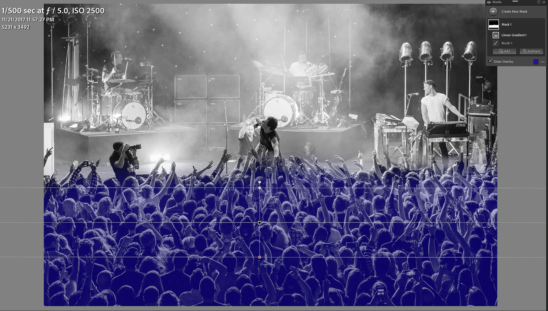 A screenshot of the Linear Gradient mask being applied to a concert photo in Adobe Lightroom. The overlay of what areas will be affected by the mask adjustments is shown in blue.