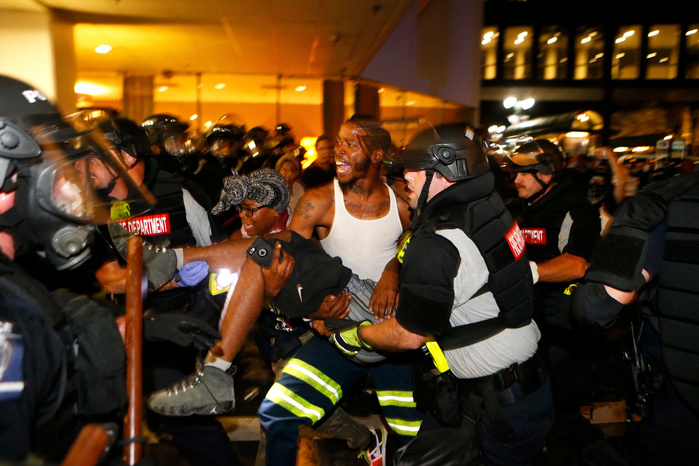 CHARLOTTE, NC - SEPTEMBER 21: Police and protesters carry a seriously wounded protester into the parking area of the the Omni Hotel during march to protest the death of Keith Scott September 21, 2016 in Charlotte, North Carolina. Keith was shot and kill