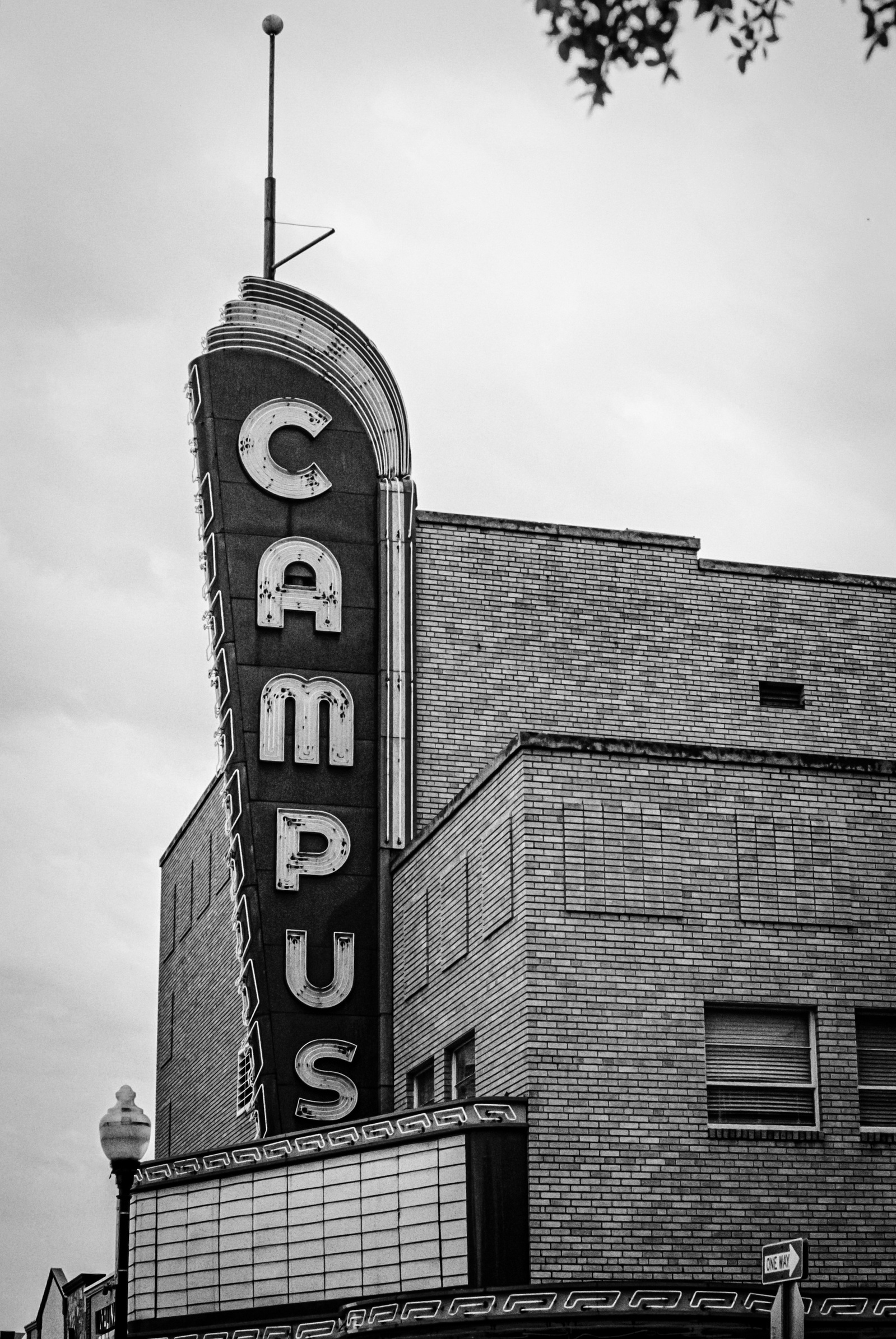 Shot in grainy black and white, the old Campus Theater sign stands like a sentry of stories. Faded neon and brick lines evoke the golden age of cinema, now paused in time.