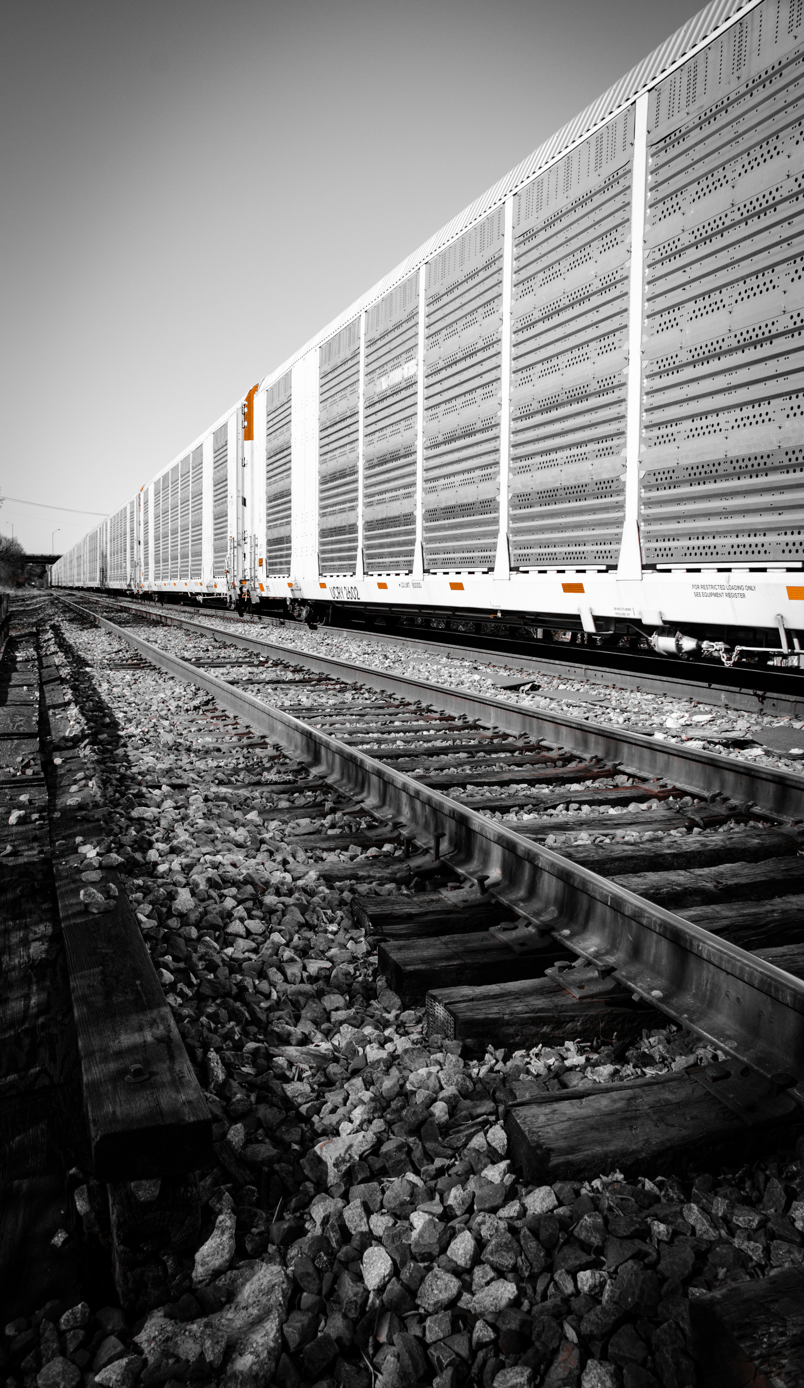 Bleached and stripped of most color, the orange trim barely lingers on the freight car. The railbed crumbles beneath it—this is movement decaying in slow time, a ghost on the tracks.