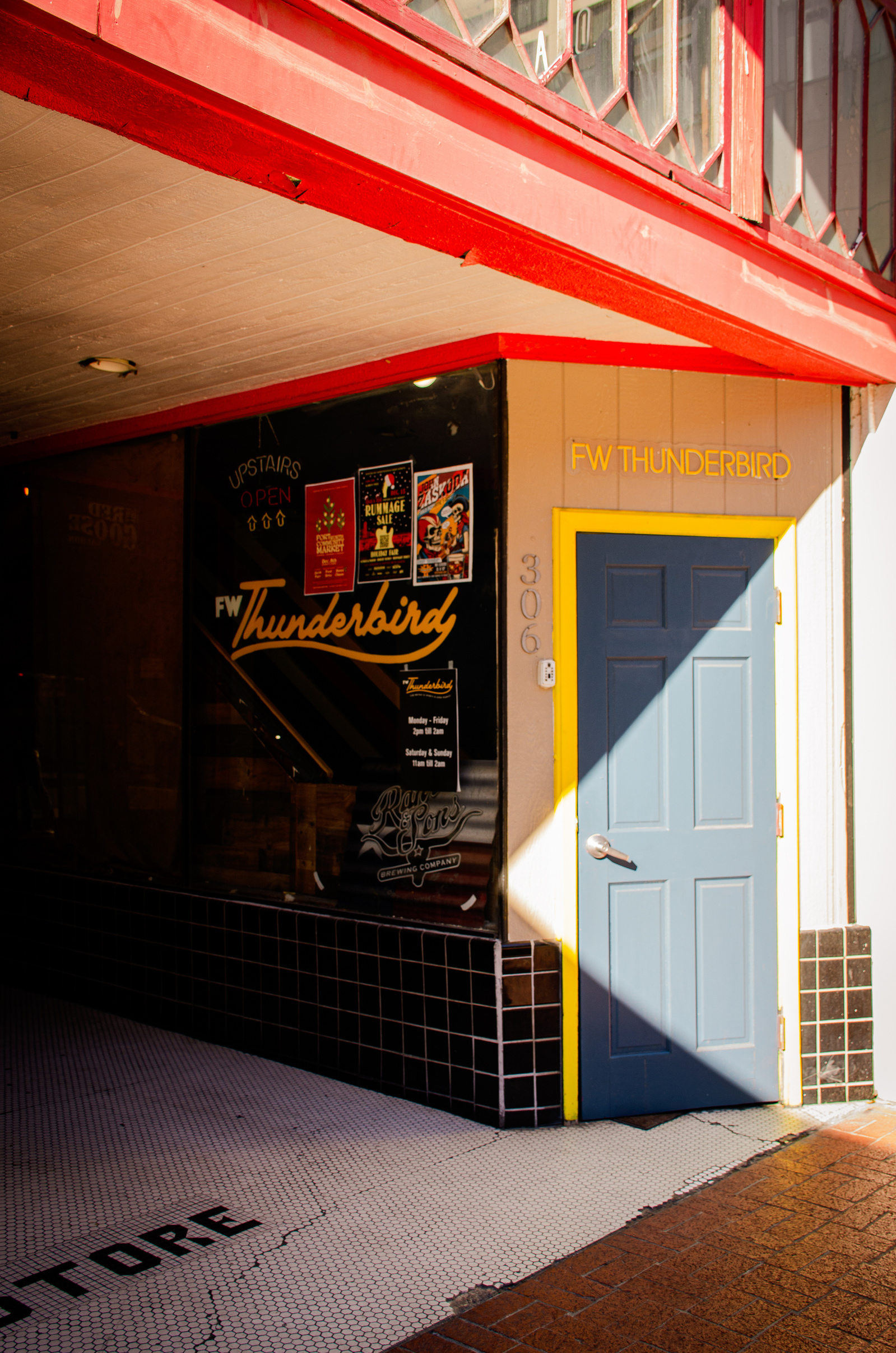 A hidden doorway under a red awning leads to the Thunderbird bar. Posters crowd the window, promising life beyond the shadow.