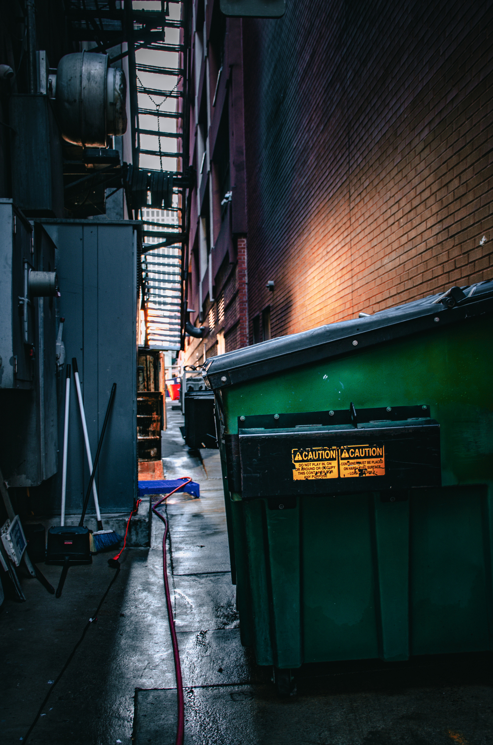 A row of green bins, boxed in by walls and shadow—an assembly line of what the city wants to forget.