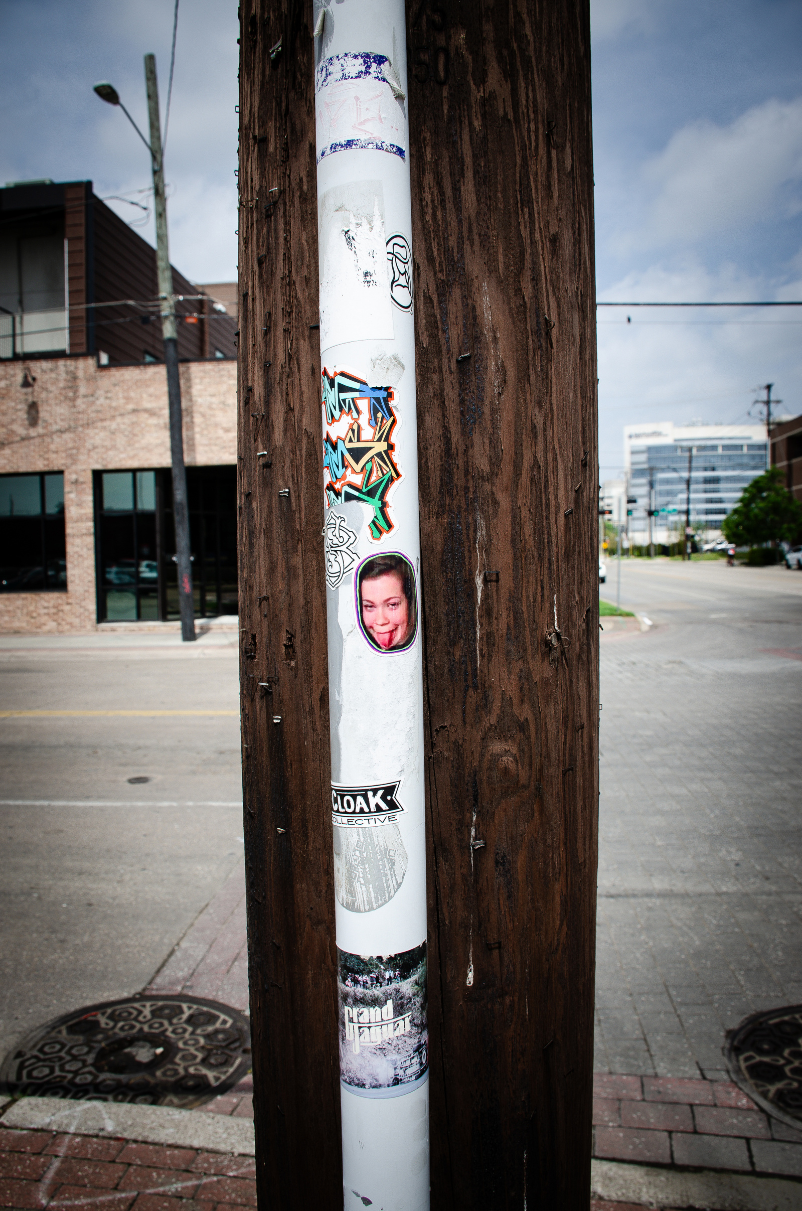 A narrow strip of rebellion. Graffiti and faces cling to a lone pole like ghosts with nowhere else to go.