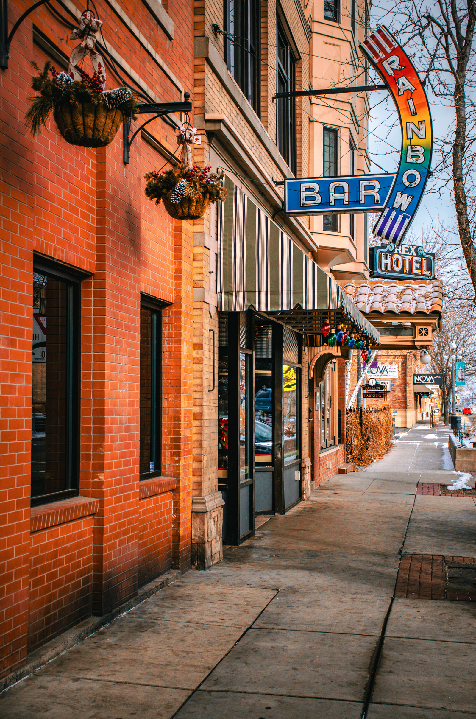 A burst of neon arcs out from the Rainbow Bar, its signage loud against a quiet street. The Rex Hotel sleeps below it—two eras sharing a single breath.