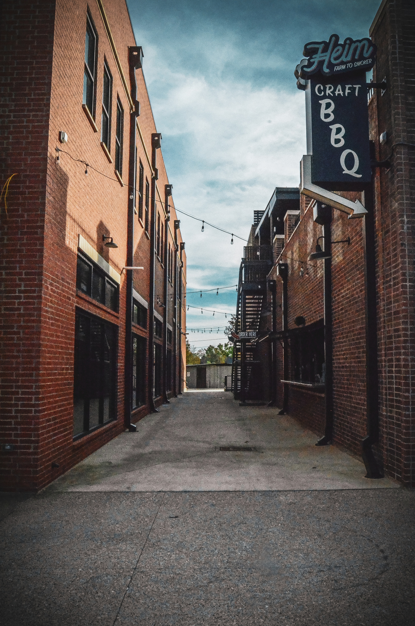 Brick walls and BBQ signage narrow into a vanishing point—an alley that tastes like char and sounds like country blues.